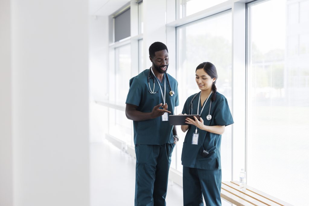 Two clinicians reviewing information on a tablet in a bright hallway.