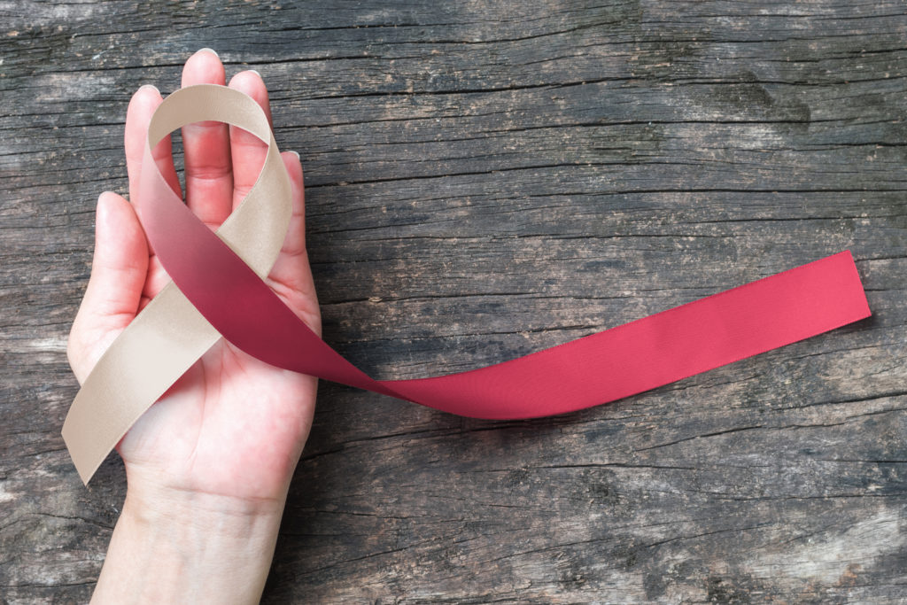 Head and neck cancer symbolic burgundy ivory white color ribbon isolated on human hand (clipping path) raising awareness help support campaign on p...