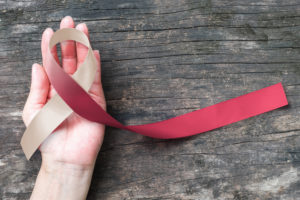 Head and neck cancer symbolic burgundy ivory white color ribbon isolated on human hand (clipping path) raising awareness help support campaign on p...