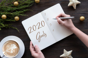 Female hands write 2020 new year resolution goal wish list in notebook on brown wooden table background, woman make notes plan for better changes s...