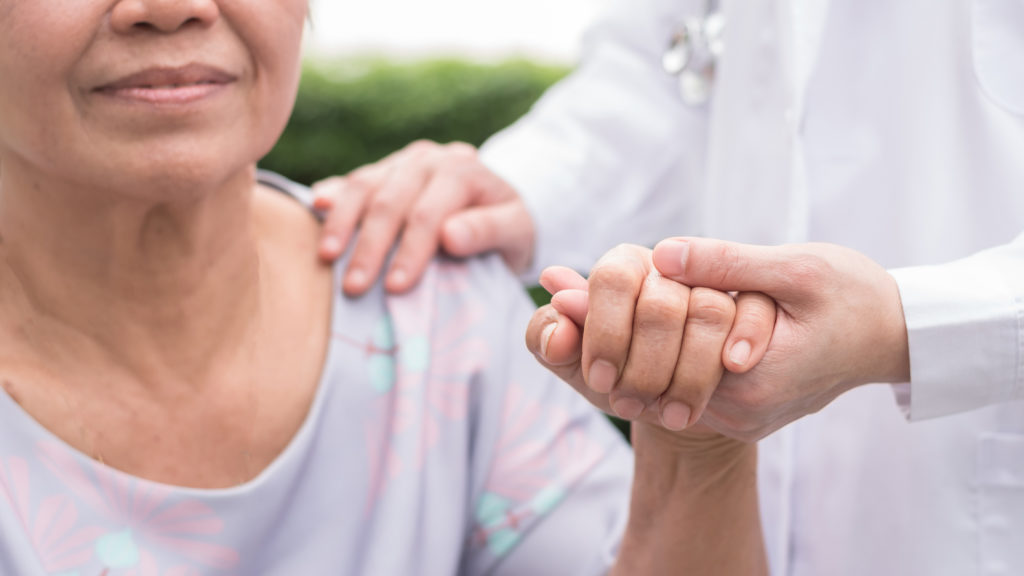 Elderly senior patient in nursing home holding doctor's hand having happy health check, medical care from hospital or caregiver service