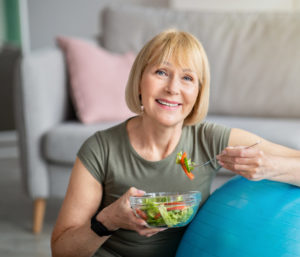 Exercise And Healthy Diet Concept. Senior Woman With Fitball Eating Fresh Vegetable Salad At Home