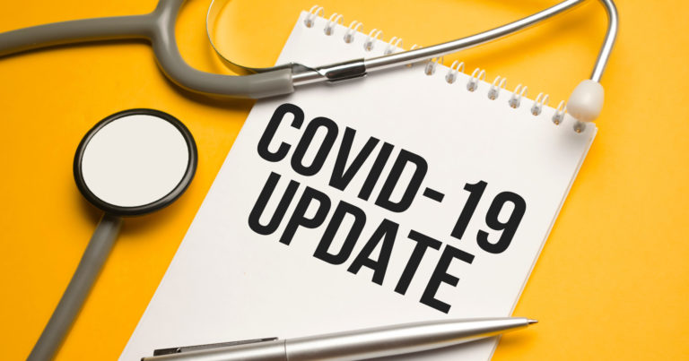 Covid 19 Update Written In Notebook On Orange Table