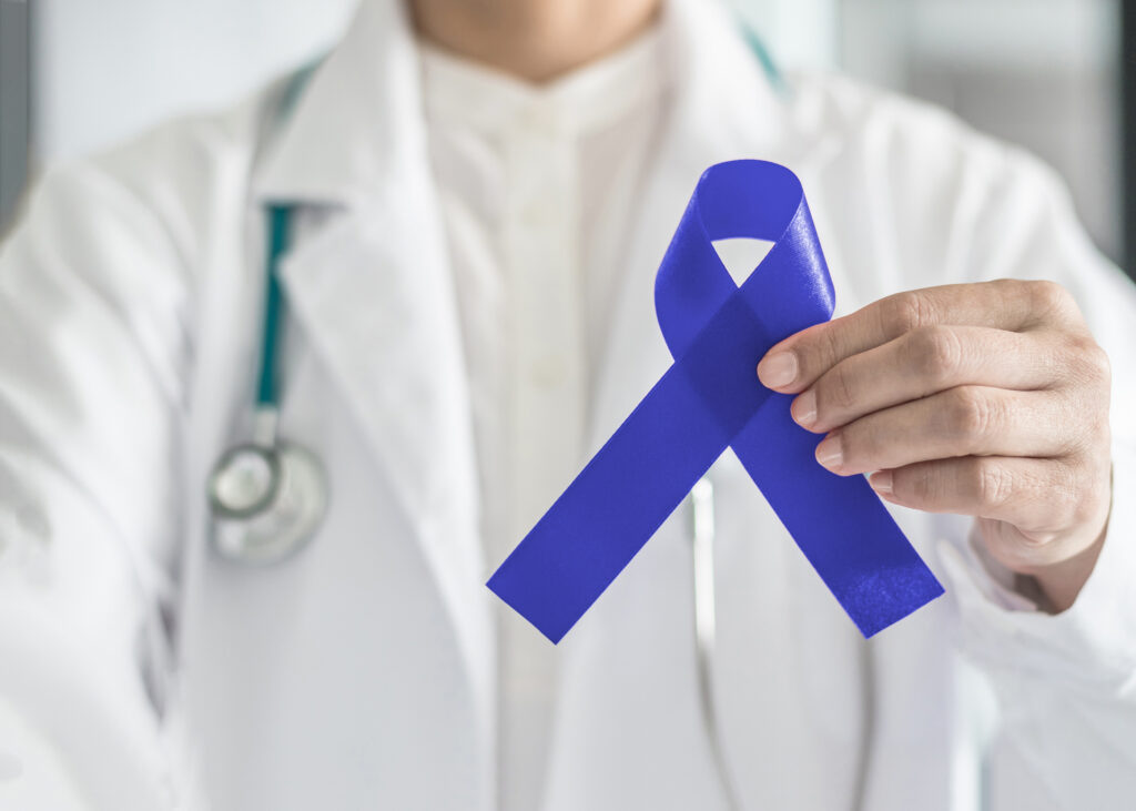 Dark blue ribbon for colon colorectal cancer awareness on medical doctor's hand support