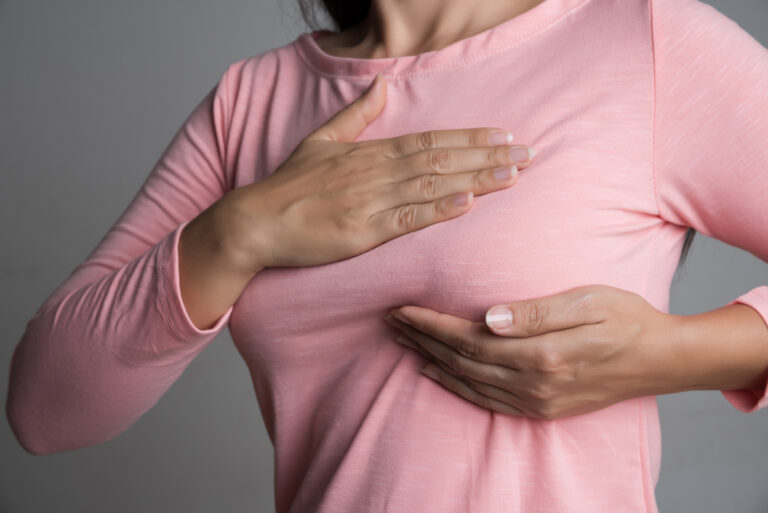 Woman hand checking lumps on her breast for signs of breast cancer on gray background. Lymphedema