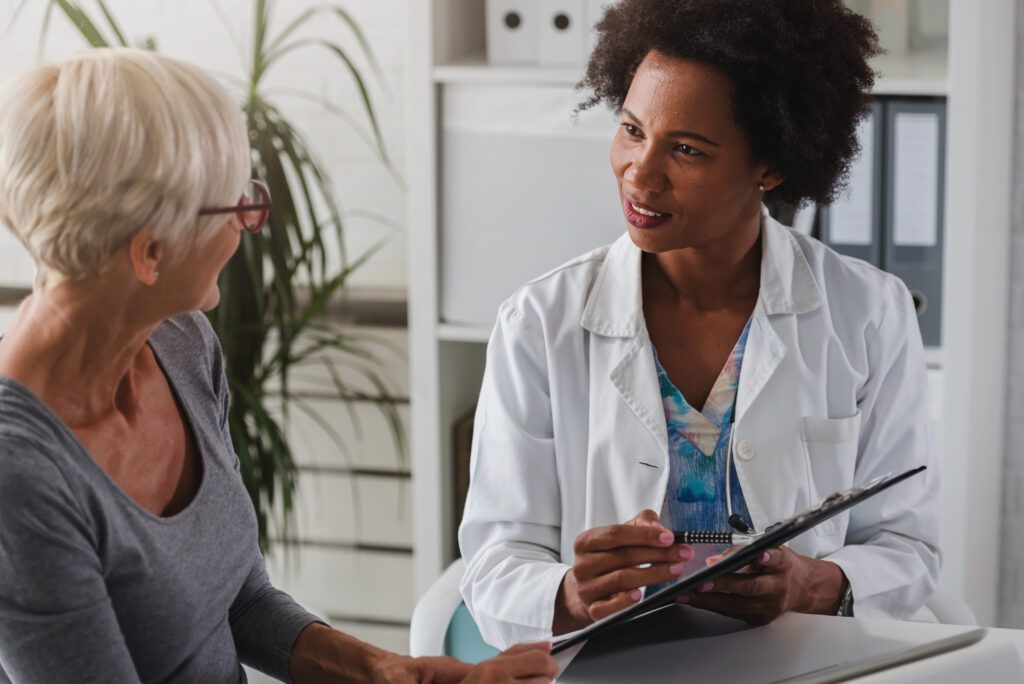 A female doctor sits at her desk and chats to an elderly female