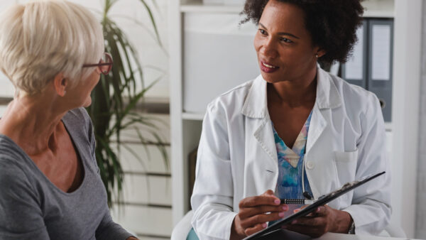 A female doctor sits at her desk and chats to an elderly female